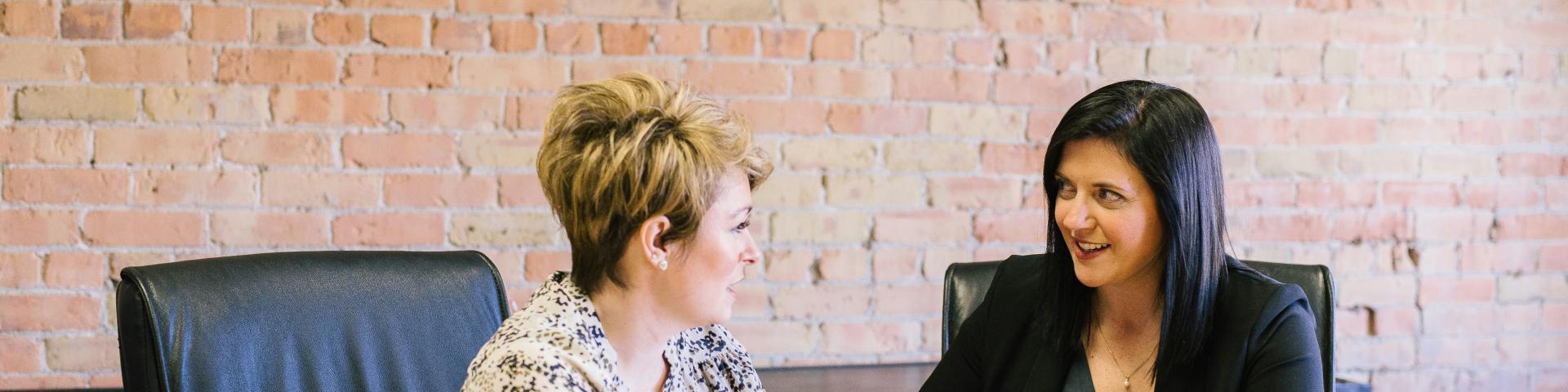 two women sitting on leather chairs in front of table