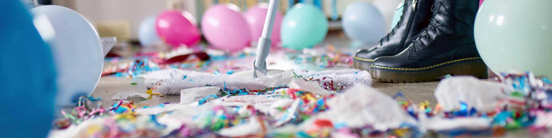 Person with pushbroom cleaning mess of floor in room after party confetti, morning after party celebration