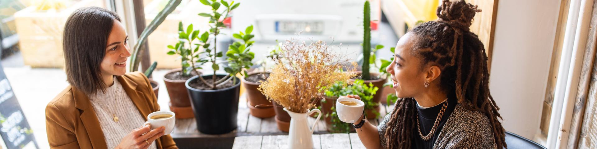 Two female business professionals having conversation over a cup of coffee at local cafe. Businesswomen talking while having coffee at a coffee shop.
