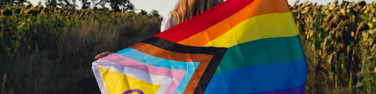 Person in a nature setting, holding a Pride flag
