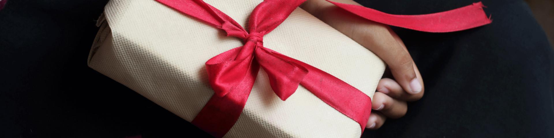 Child's hands holding a wrapped gift tied with a red ribbon.