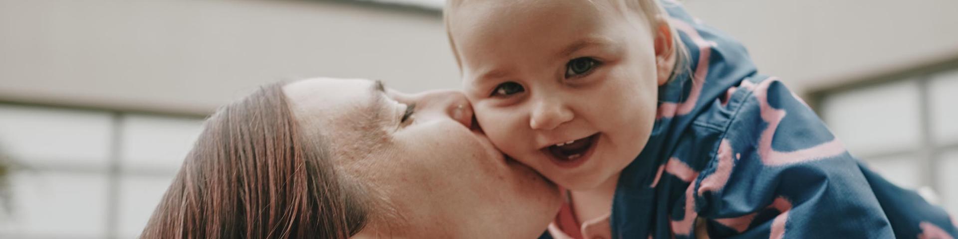 Mom holding baby in the air and kissing him on the cheek