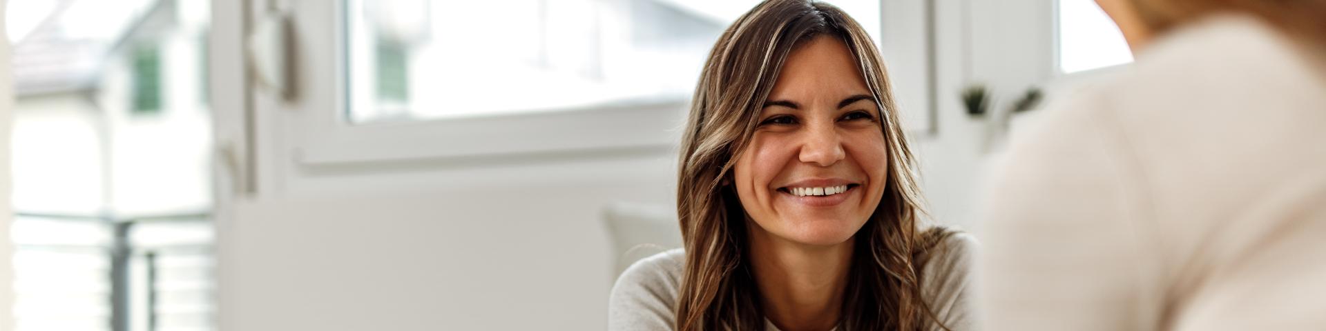 Smiling woman sitting opposite another woman, who is facing away from the camera.