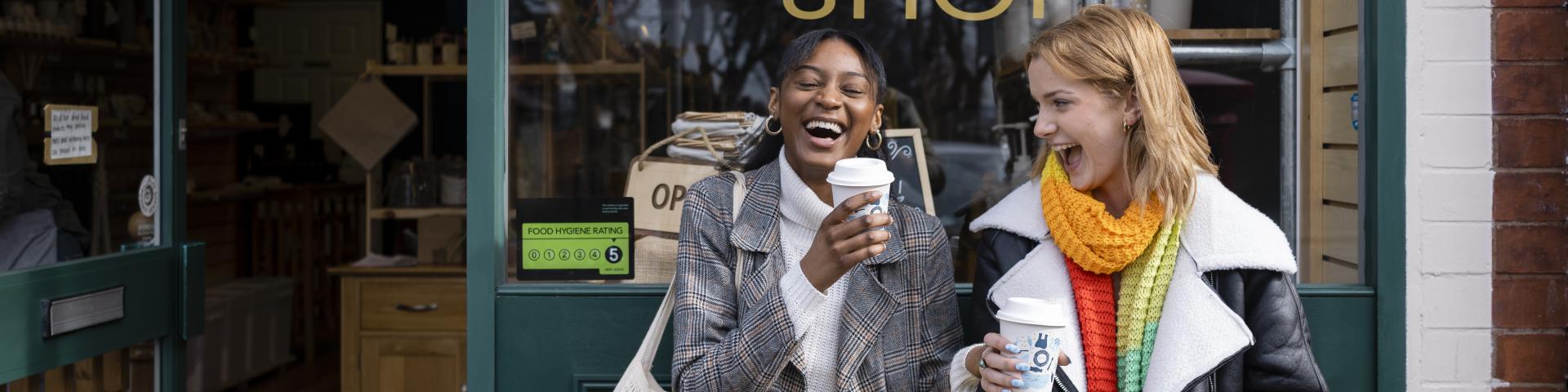 Two friends sitting outside a store having coffee and treats