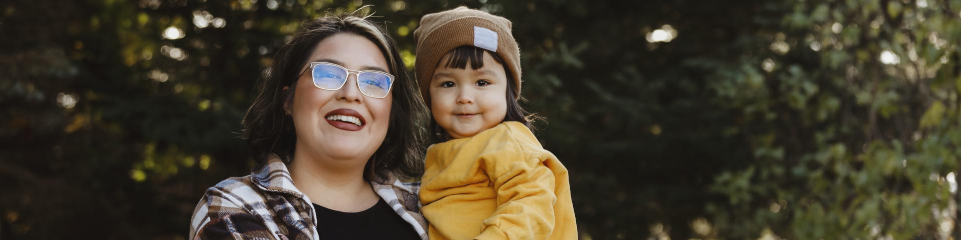 An image of an Indigenous two~year~old girl and her mother, outside.