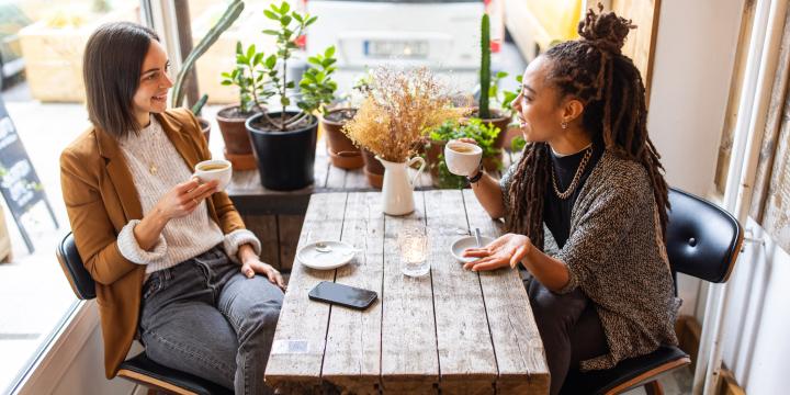 Two female business professionals having conversation over a cup of coffee at local cafe. Businesswomen talking while having coffee at a coffee shop.