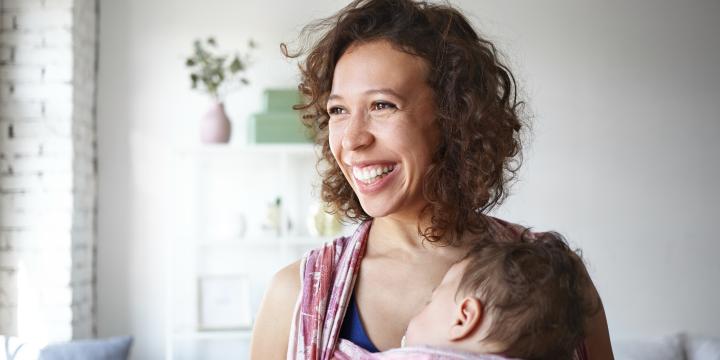 Smiling women carrying a sleeping baby on a sling 