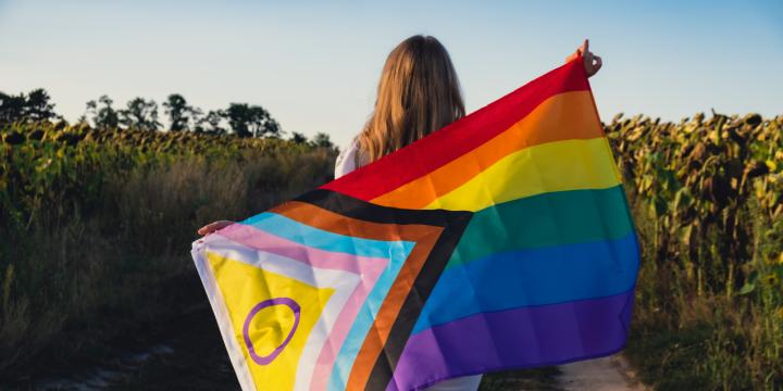 Person in a nature setting, holding a Pride flag