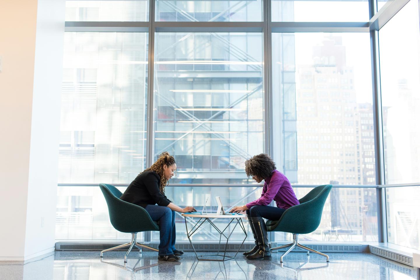 Two females sitting on dark grey chairs looking at their computers