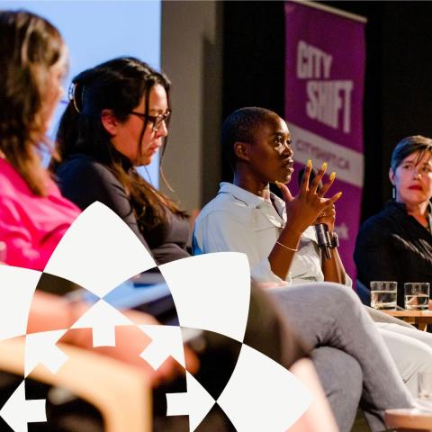 A panel of diverse leaders sitting at the front of the stage while one of them is talking.