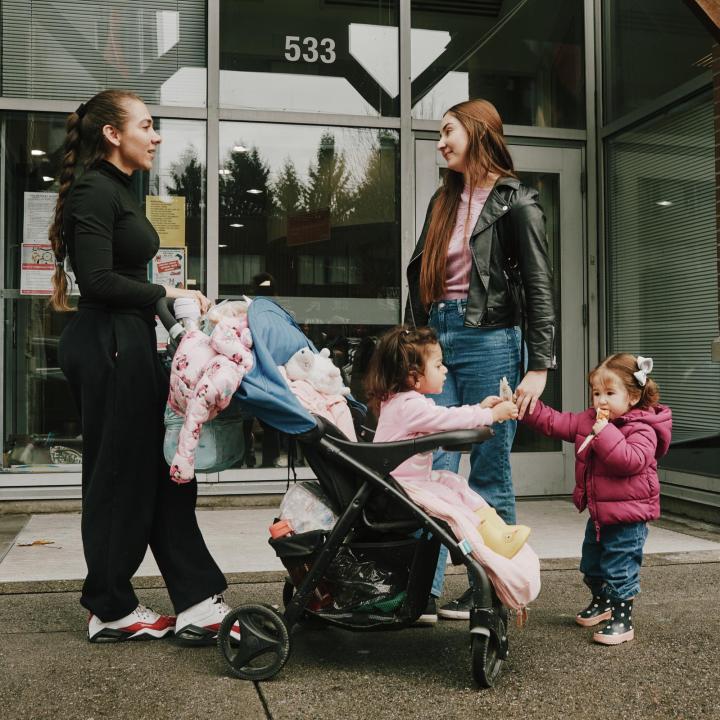 Two young moms talking to each other while their toddlers interact